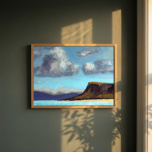 Fair Head from the Sea framed print in a natural oak frame on a dark green wall beside a window, dappled plant shadow