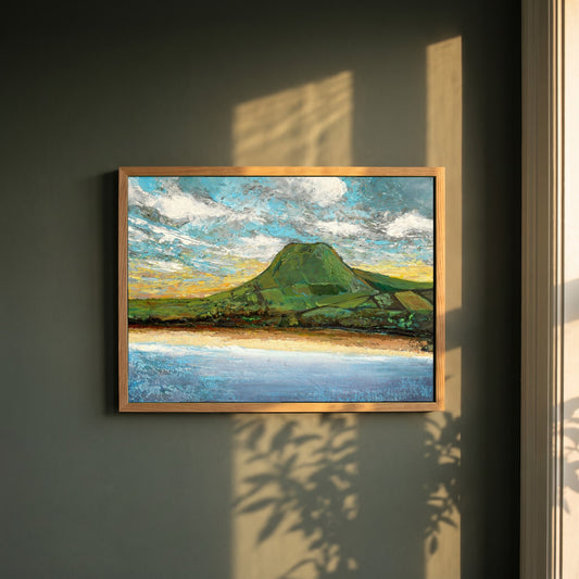 Lurig Mountain at Sunset framed print in a natural oak frame on a dark green wall beside a window, dappled plant shadow