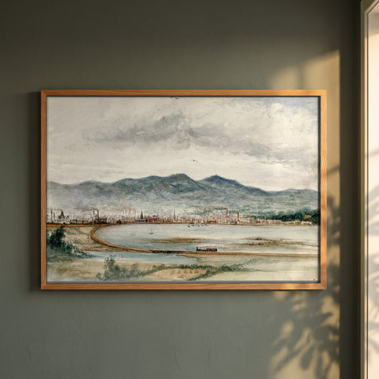 Belfast from Bunker's Hill by John O'Connor framed print in a natural oak frame on a dark green wall beside a window, dappled plant shadow