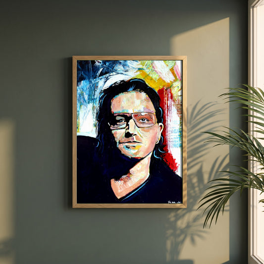 Vibrant Bono U2 framed print in a natural oak frame on a dark green wall beside a window, dappled plant shadow