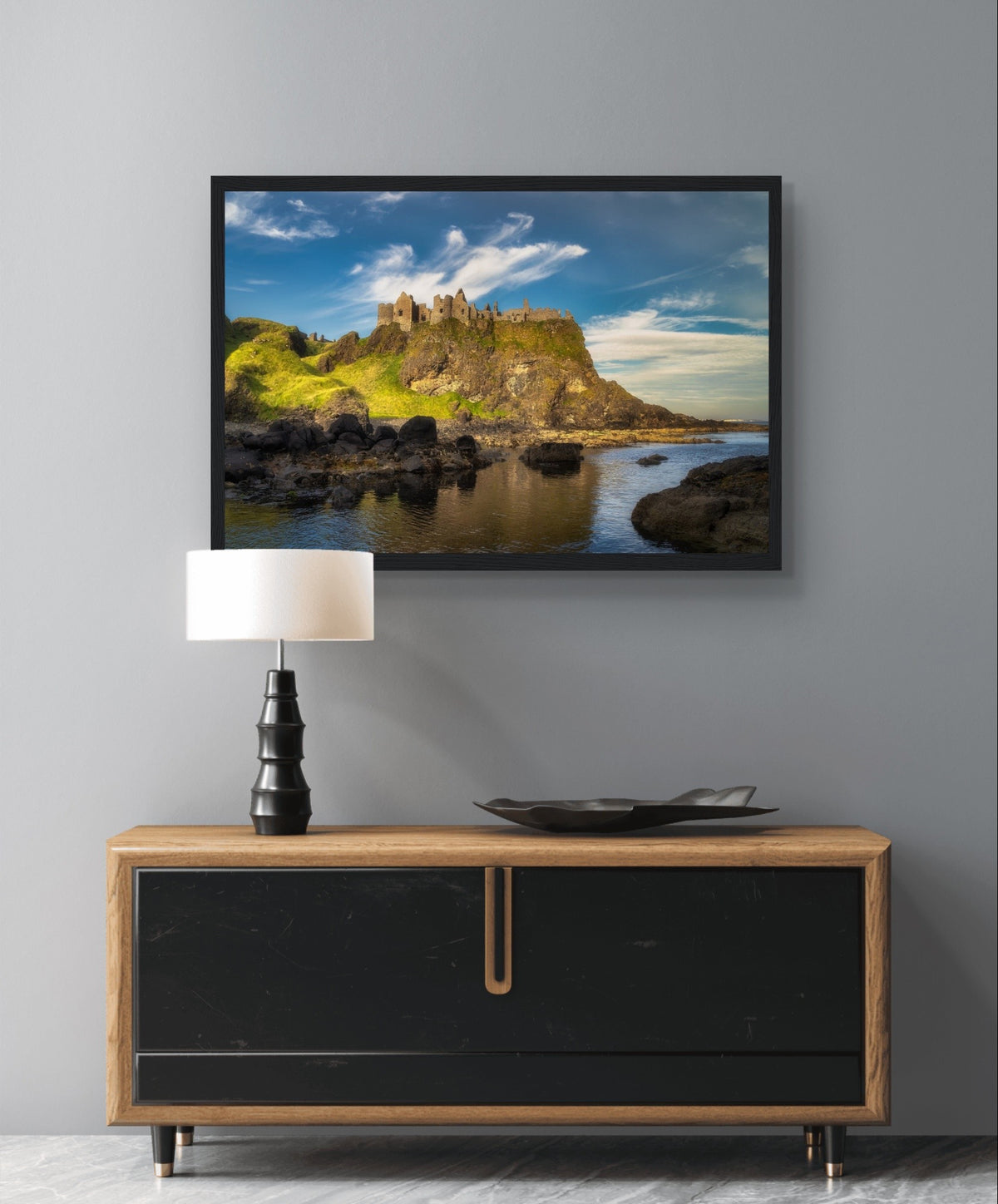 Dunluce Castle cliffs print in a black frame above a cabinet with a table lamp
