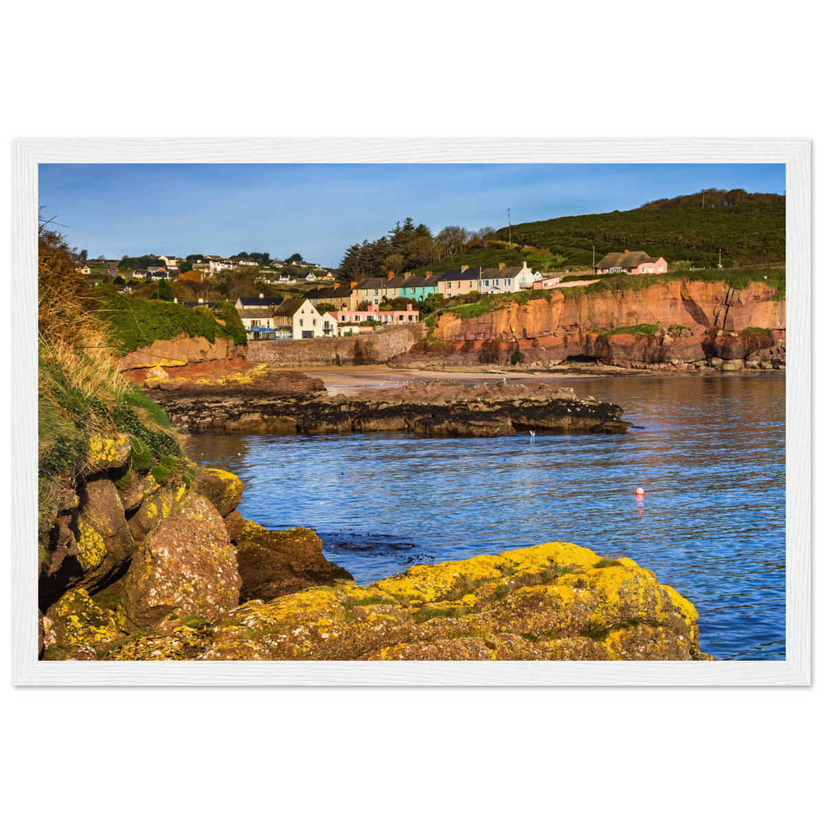 Dunmore East coastline photograph in a textured white frame, calm blue water and red sandstone