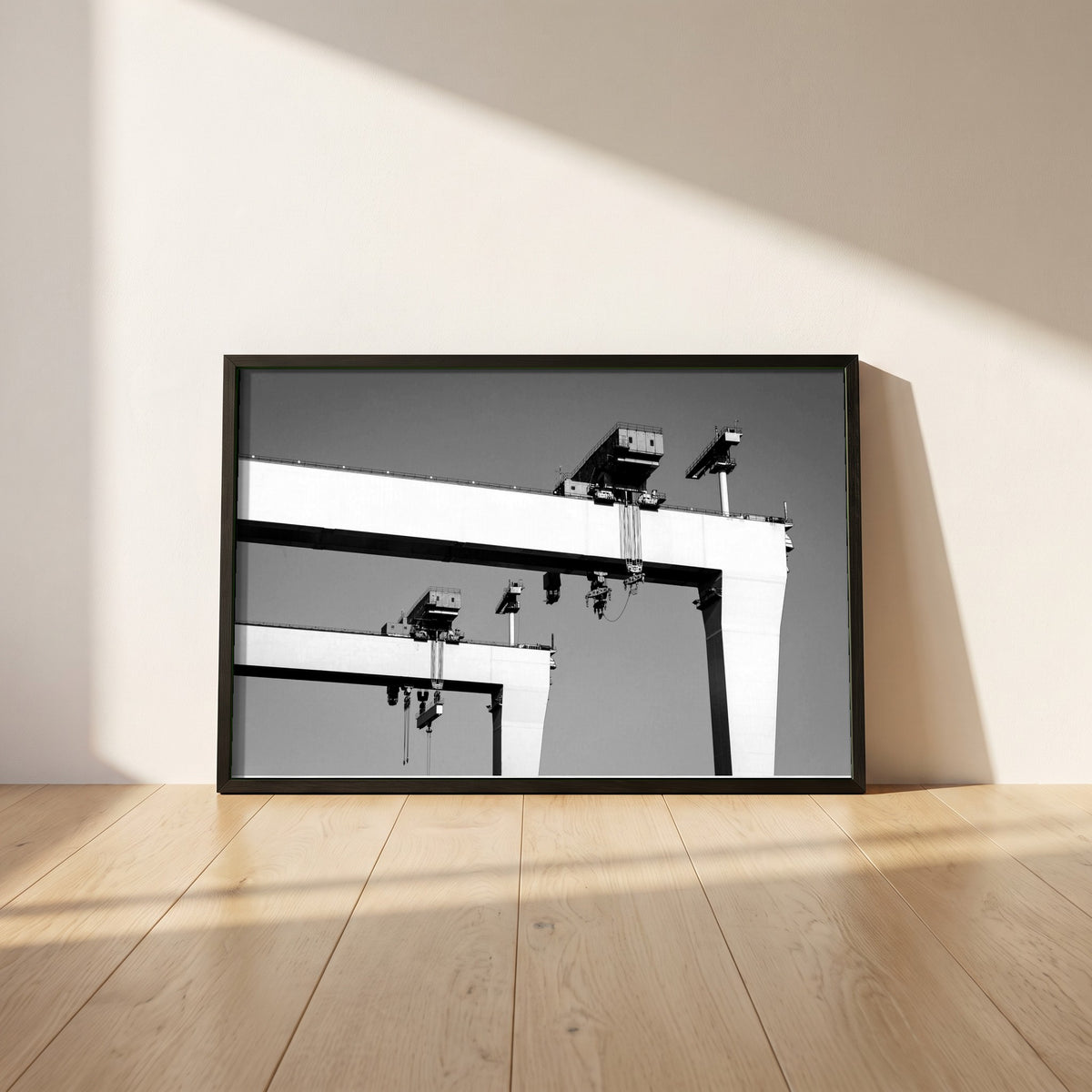Harland & Wolff Cranes, Belfast framed print in a black frame leaning against a white plaster wall on oak floorboards in morning light