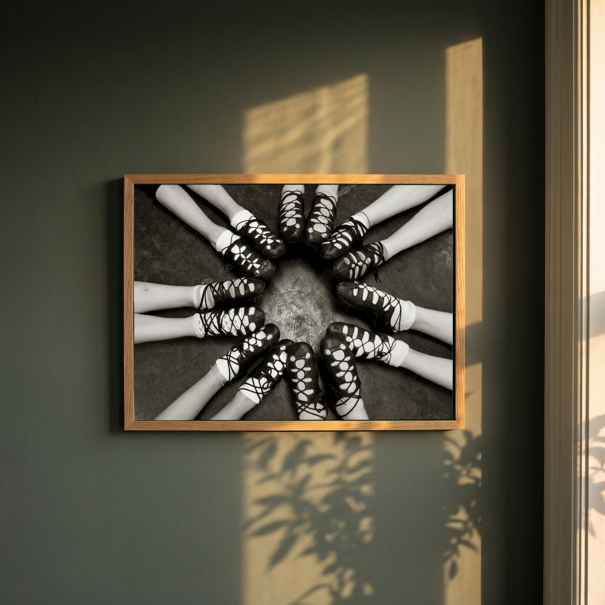 Irish Dancing Shoes Black & White framed print in a natural oak frame on a dark green wall beside a window, dappled plant shadow