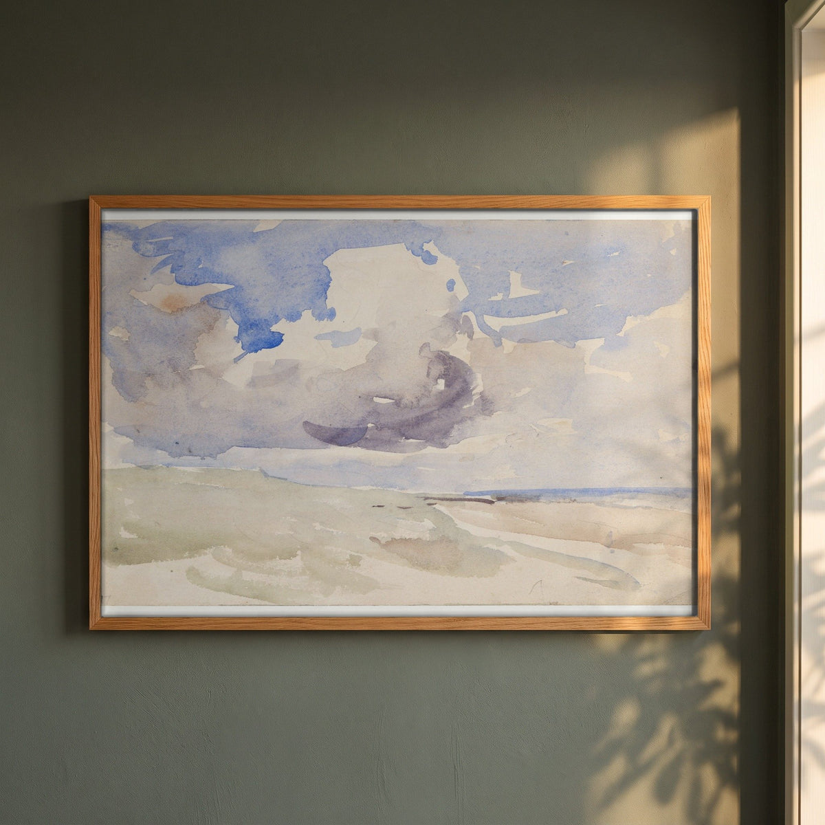 Low Clouds over a Beach framed print in a natural oak frame on a dark green wall beside a window, dappled plant shadow