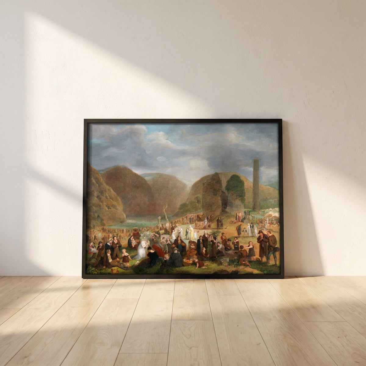 Patron's Day at the Seven Churches, Glendalough (c.1816) framed print in a black frame leaning against a white plaster wall on oak floorboards in morning light