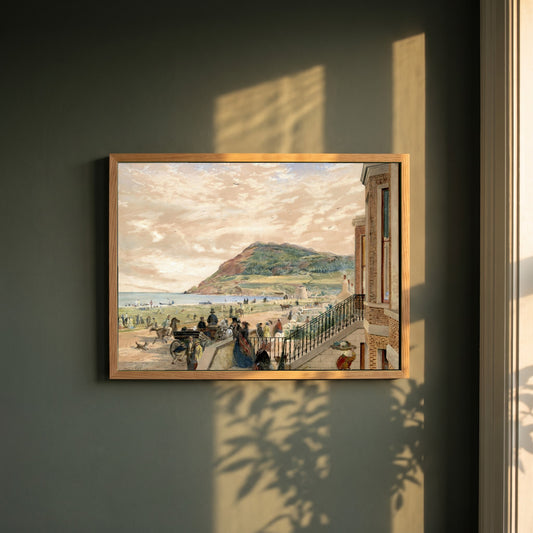 The Seafront at Bray framed print in a natural oak frame on a dark green wall beside a window, dappled plant shadow