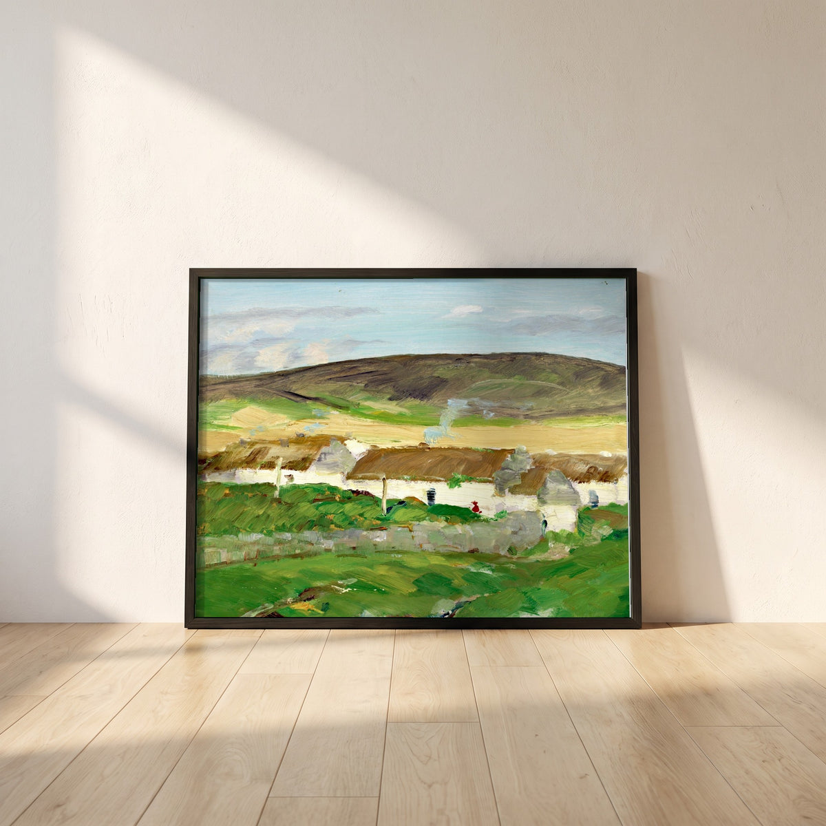 The White Cottage framed print in a black frame leaning against a white plaster wall on oak floorboards in morning light